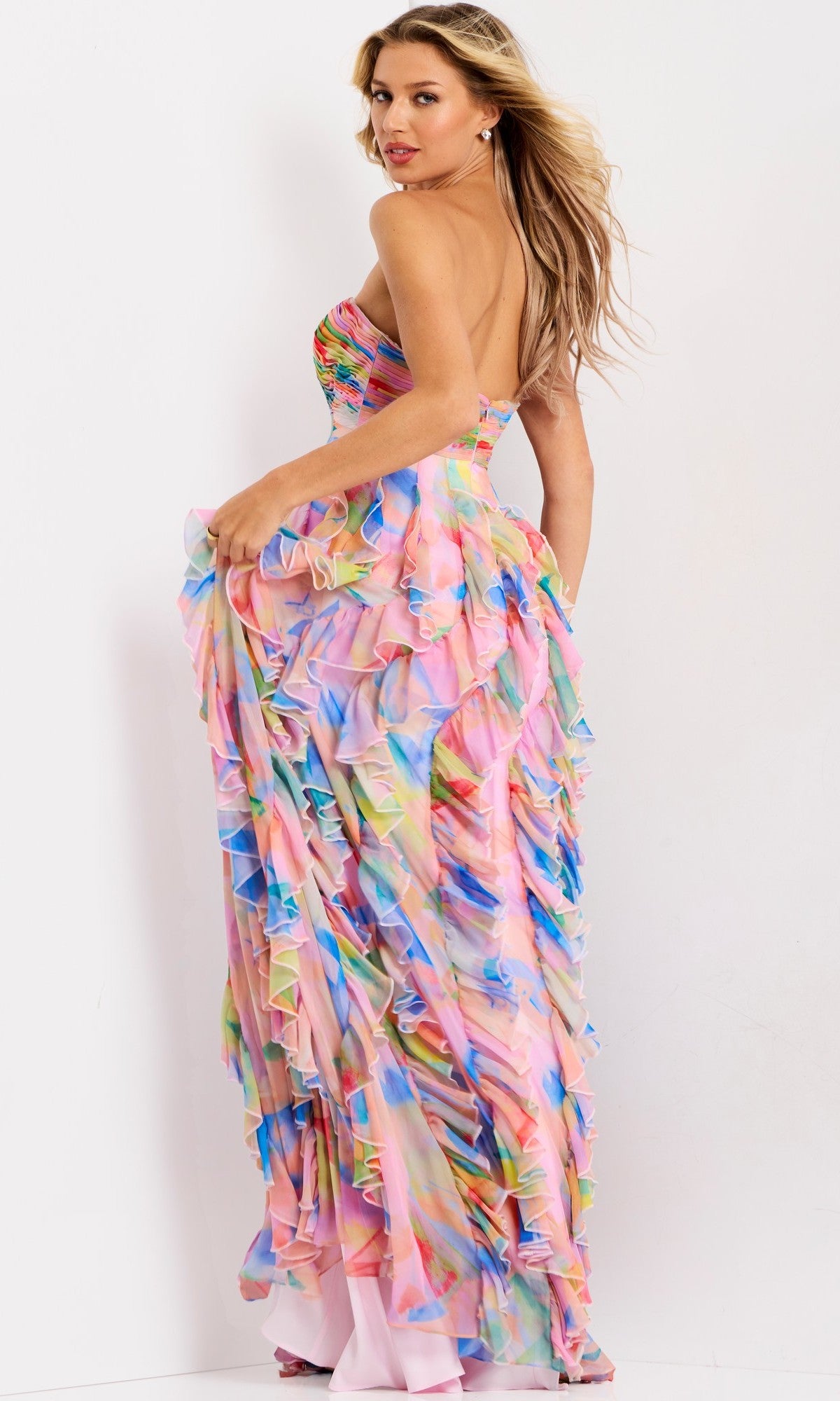 A woman poses in the Jovani 46381 long prom dress, a strapless chiffon gown with ruffles, a multicolored abstract pattern, and an open back, set against a plain white background.
